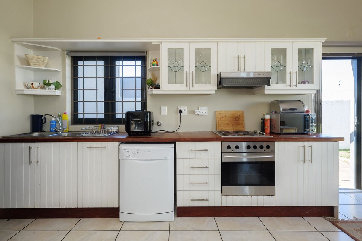 A functional kitchen featuring white cabinetry, a warm wooden countertop, built-in oven, hob, extractor fan, and tiled flooring with direct access to the exterior.