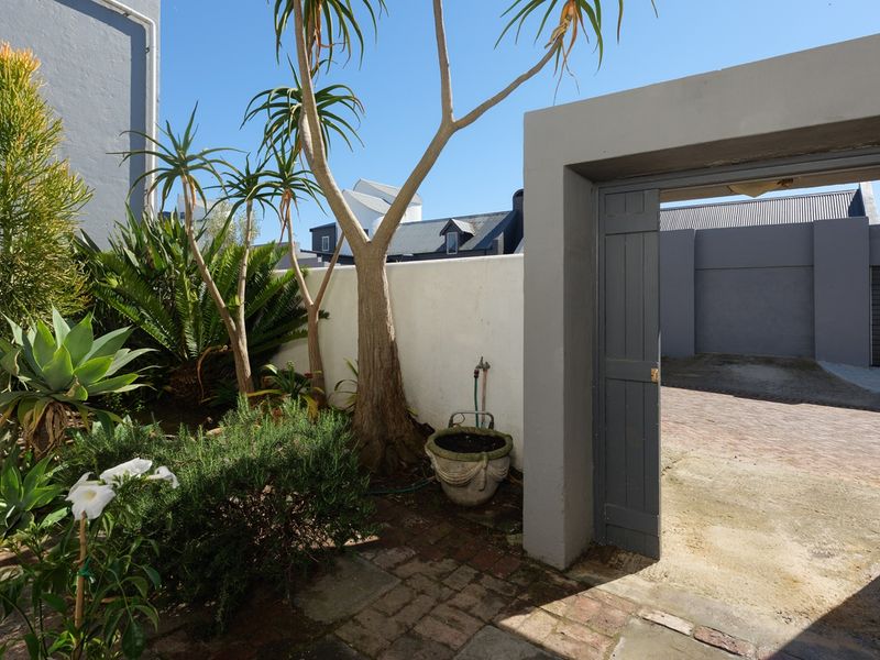 A private rear courtyard area featuring brick paving, established garden beds, and a secure pedestrian gate leading to the driveway.