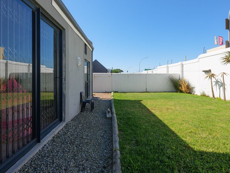 A private rear garden featuring a lawn, gravel pathway, and secure perimeter wall with electric fencing, accessible via sliding glass doors.