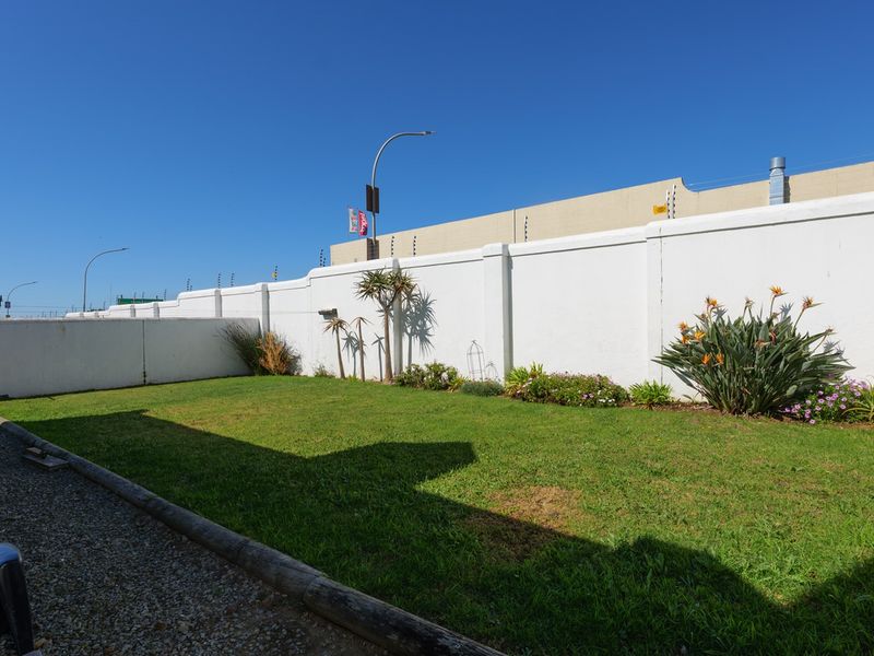 A private rear garden featuring a well-maintained lawn, gravel border, and high perimeter walls with integrated electric fencing for added security.