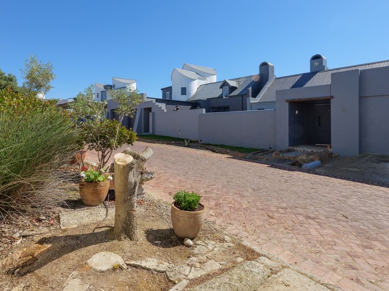 Street view of the townhouse complex entrance featuring brick paving, grey boundary walls, and modern architectural roof lines.