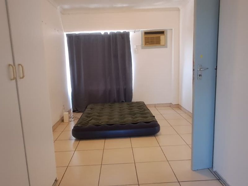 A bedroom featuring tiled flooring, built-in cupboards, and a window-mounted air conditioning unit, presenting a blank canvas for potential renovation or staging.