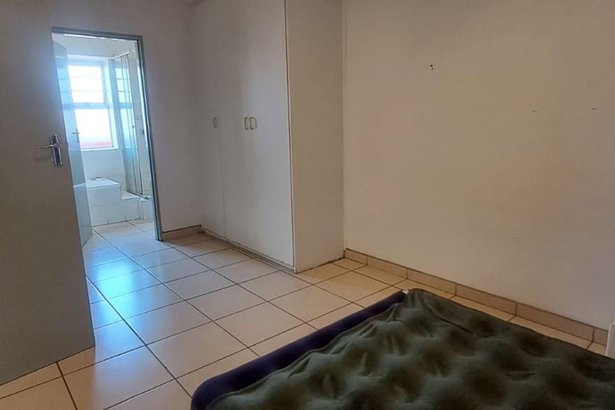 A bedroom featuring tiled flooring and built-in cupboards, with an adjoining en-suite bathroom. The space requires cosmetic updates to improve its overall condition.