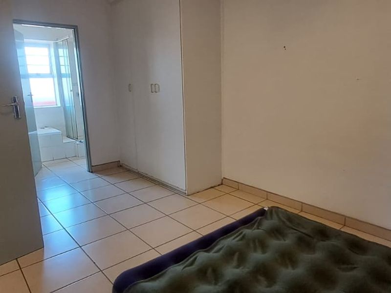 A bedroom featuring tiled flooring and built-in cupboards, with an adjoining en-suite bathroom. The space requires cosmetic updates to improve its overall condition.