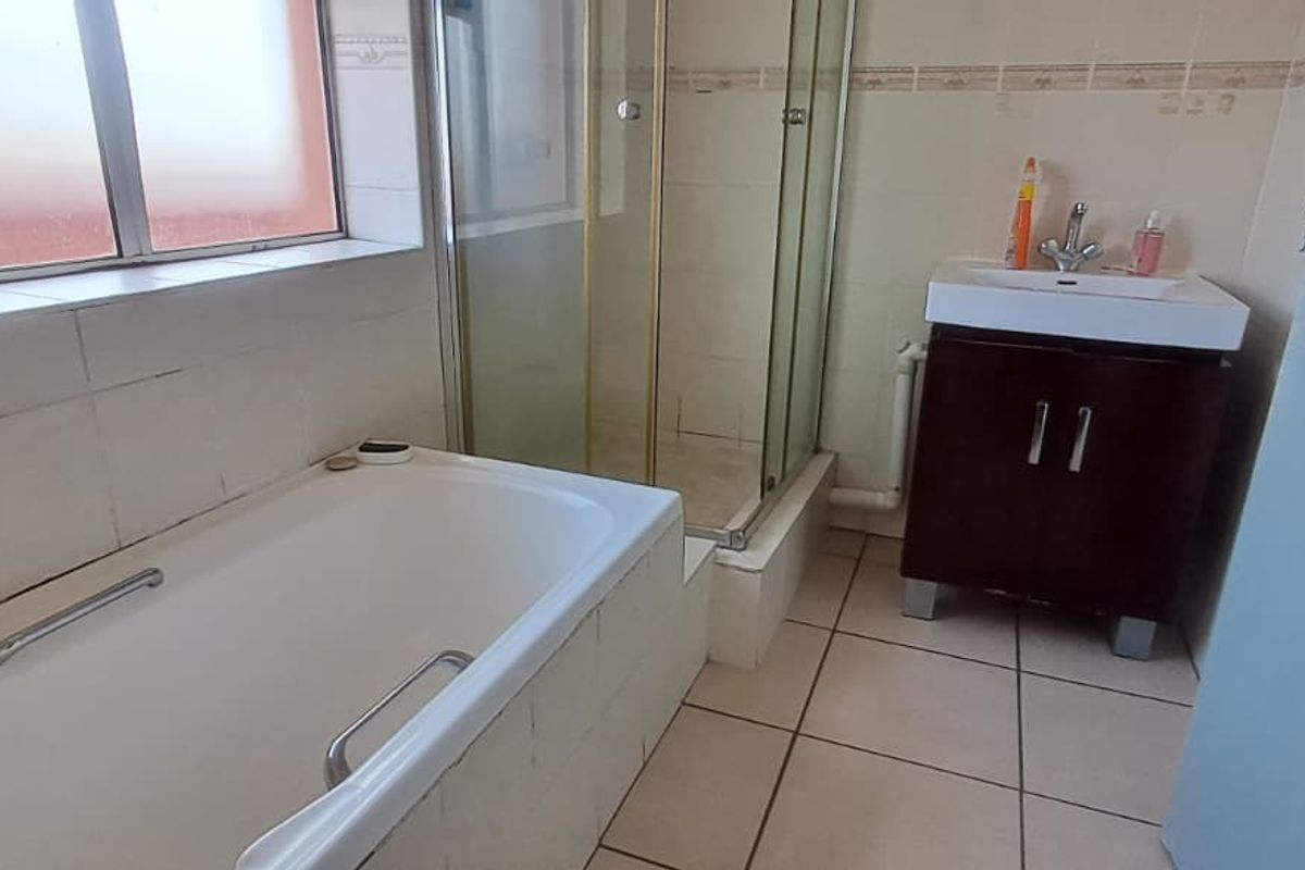A functional bathroom featuring a bathtub, separate shower enclosure, and a vanity basin with tiled finishes throughout.