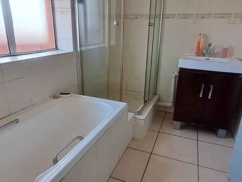 A functional bathroom featuring a bathtub, separate shower enclosure, and a vanity basin with tiled finishes throughout.