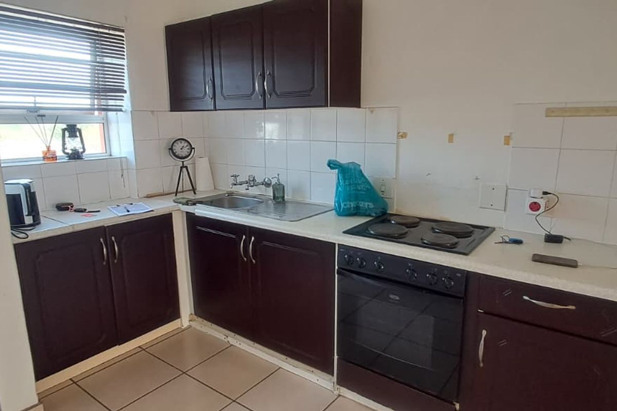 Compact kitchen featuring dark wood cabinetry, built-in electric oven and hob, tiled backsplash, and tiled flooring, offering a functional layout for renovation.