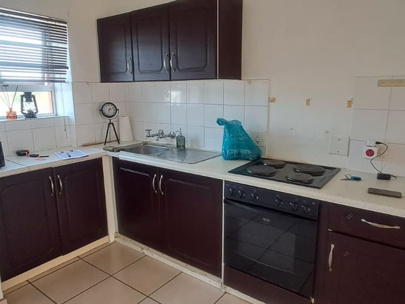 Compact kitchen featuring dark wood cabinetry, built-in electric oven and hob, tiled backsplash, and tiled flooring, offering a functional layout for renovation.