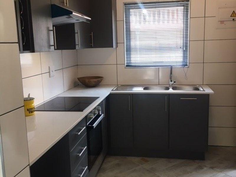 Modern kitchen featuring dark cabinetry, white countertops, integrated electric hob and oven, stainless steel sink, and neutral tiled flooring.