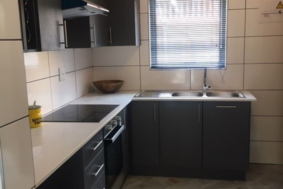 Modern kitchen featuring dark cabinetry, white countertops, integrated electric hob and oven, stainless steel sink, and neutral tiled flooring.
