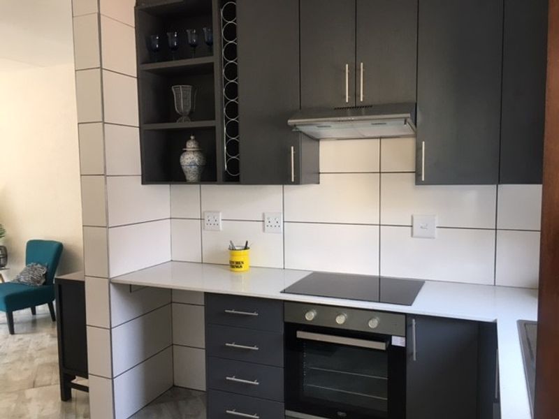 Modern kitchen featuring dark grey cabinetry, stone countertops, built-in oven, electric hob, and a tiled backsplash with integrated wine storage.