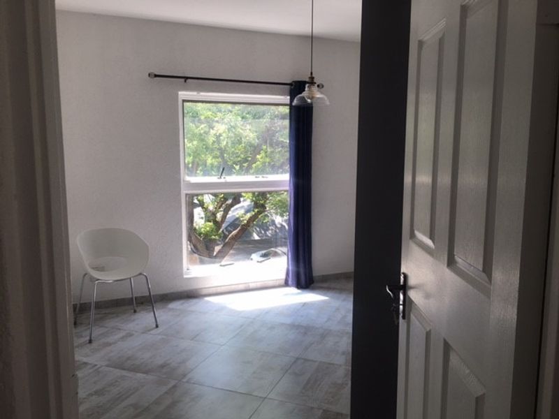 A bright, empty bedroom featuring tiled flooring, a single pendant light, and a window with a curtain rod.