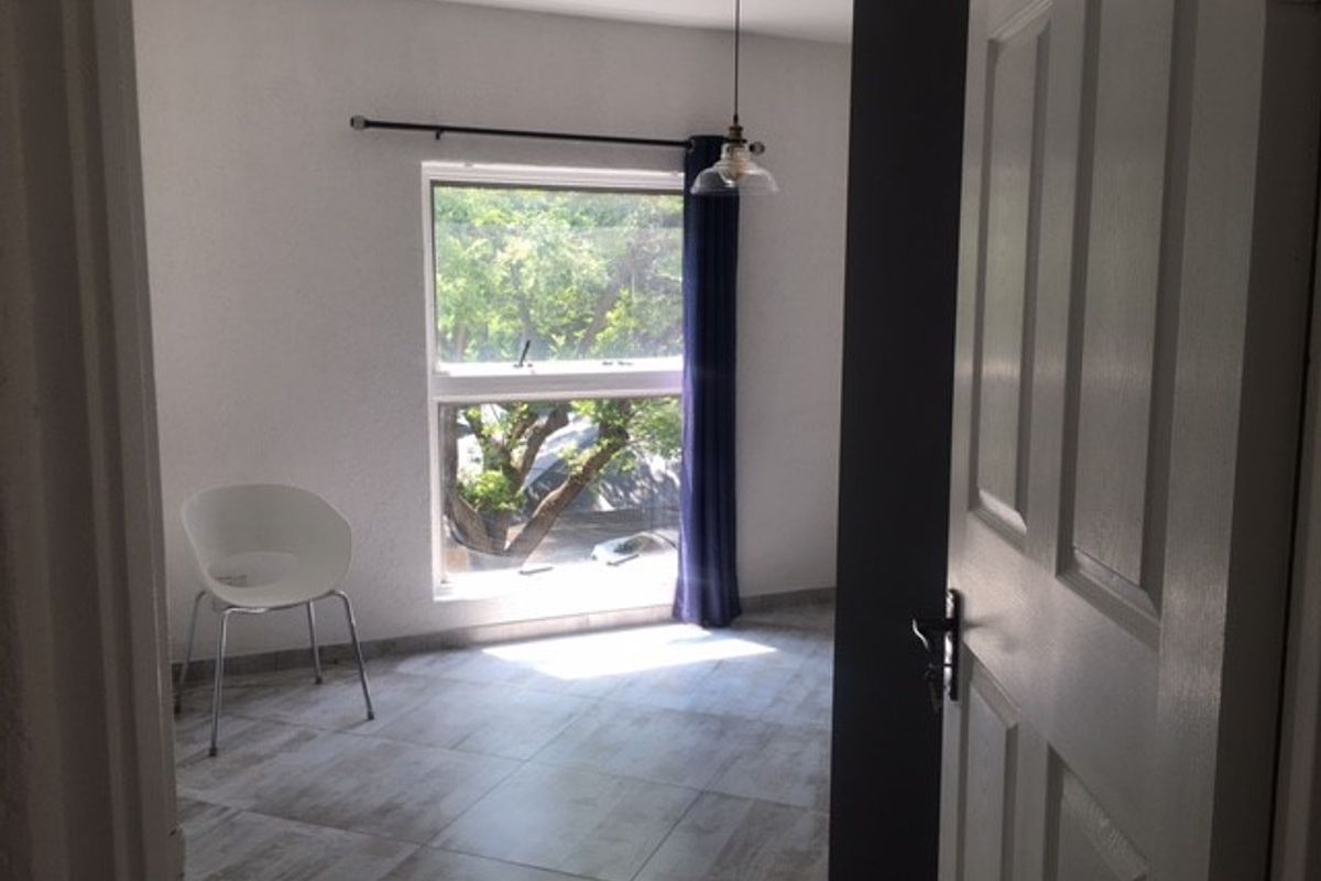 A bright, empty bedroom featuring tiled flooring, a single pendant light, and a window with a curtain rod.