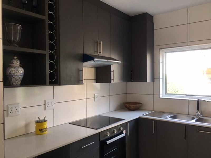Modern kitchen featuring dark cabinetry, stone countertops, integrated hob and oven, stainless steel sink, and a tiled backsplash with ample storage space.