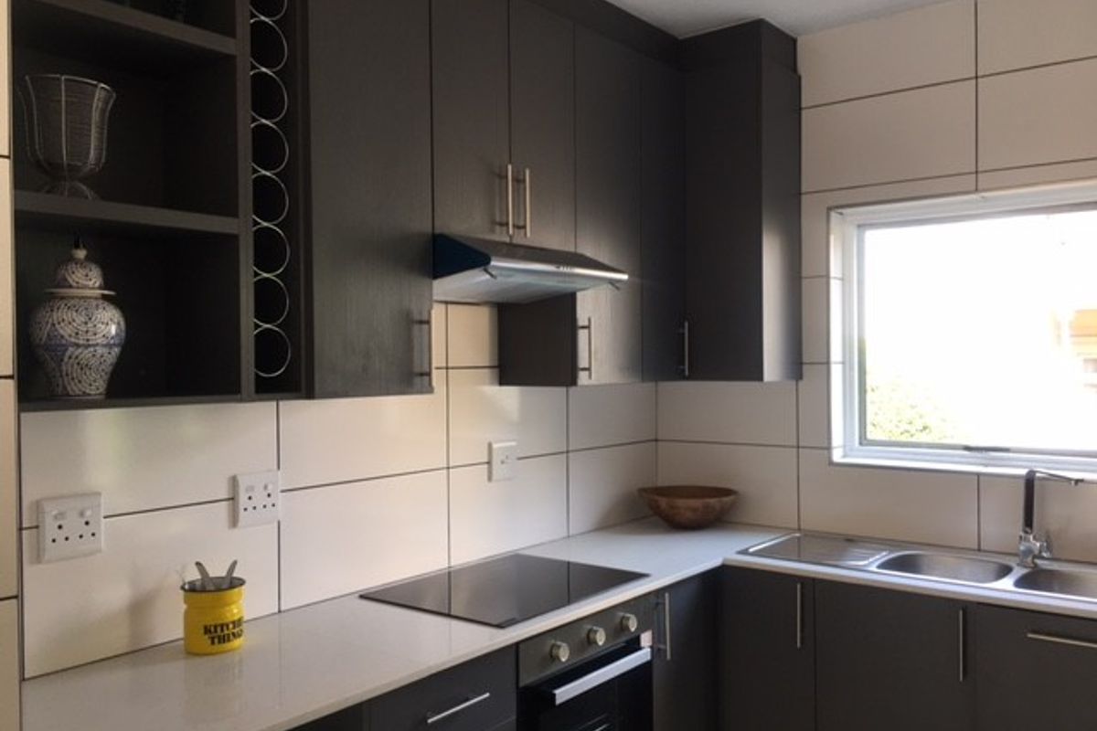 Modern kitchen featuring dark cabinetry, stone countertops, integrated hob and oven, stainless steel sink, and a tiled backsplash with ample storage space.
