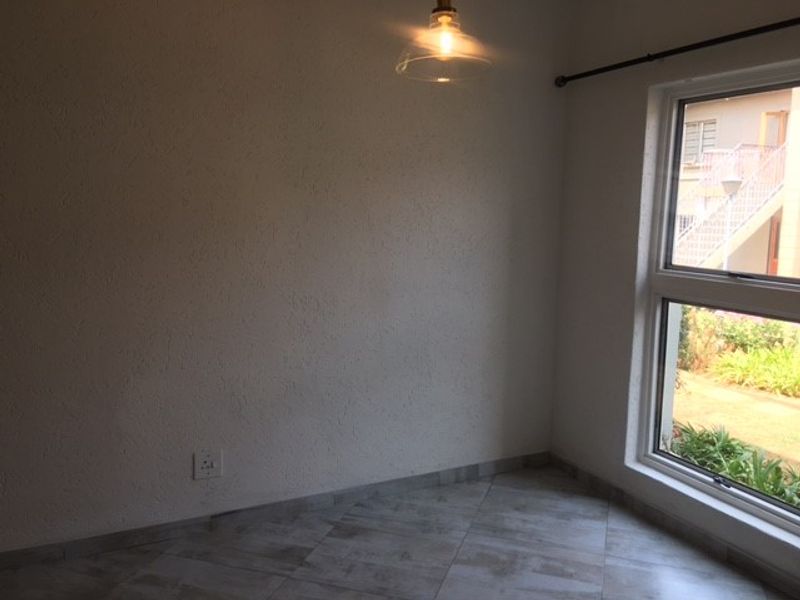 A bright, empty bedroom featuring tiled flooring, textured walls, and a large aluminium-framed window providing natural light.