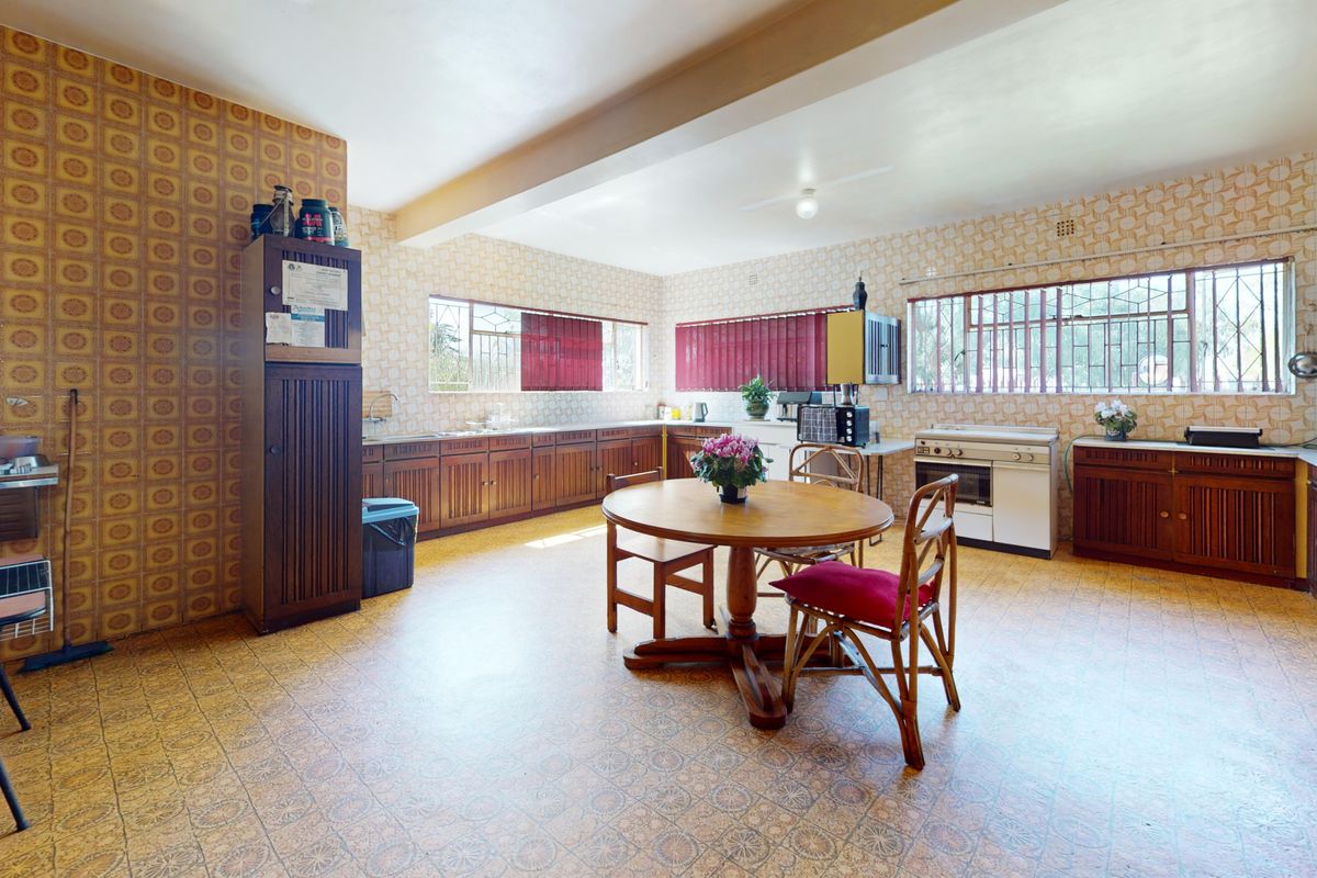 Spacious kitchen featuring extensive wooden cabinetry, a freestanding stove, and large windows with security bars, offering significant potential for modernization.