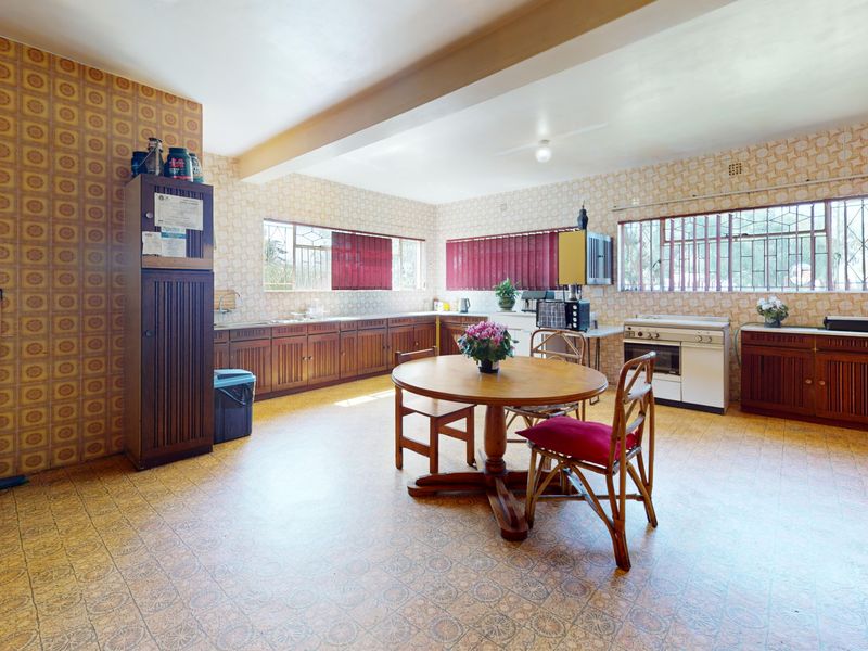 Spacious kitchen featuring extensive wooden cabinetry, a freestanding stove, and large windows with security bars, offering significant potential for modernization.