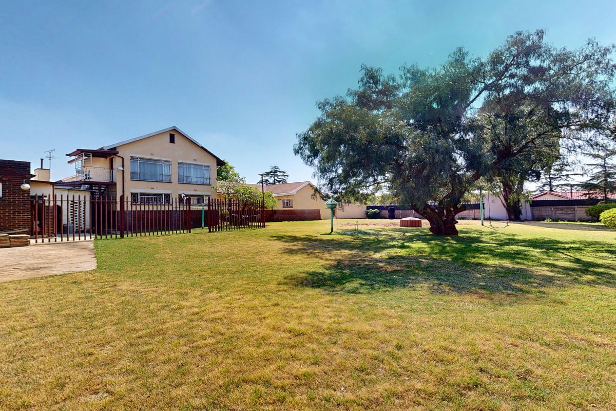 Spacious rear garden featuring a large mature tree, concrete patio area, and secure metal perimeter fencing surrounding the residential property.