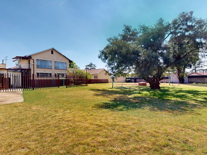 Spacious rear garden featuring a large mature tree, concrete patio area, and secure metal perimeter fencing surrounding the residential property.