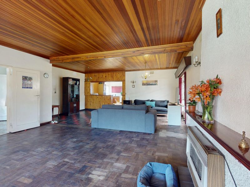 Spacious open-plan living area featuring a distinctive timber tongue and groove ceiling, parquet flooring, and a built-in wall heater.
