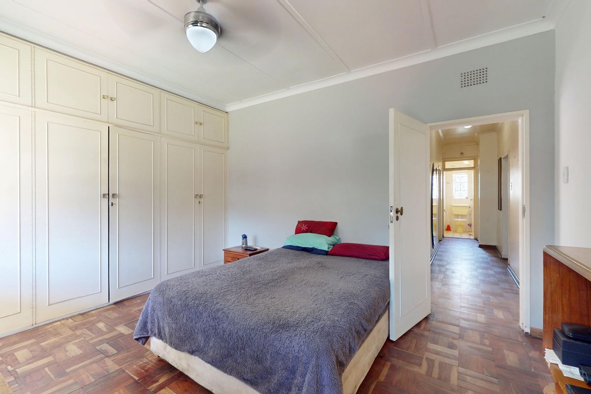 A bedroom featuring classic parquet flooring, extensive built-in cabinetry, and a ceiling fan, with a view leading into the hallway.