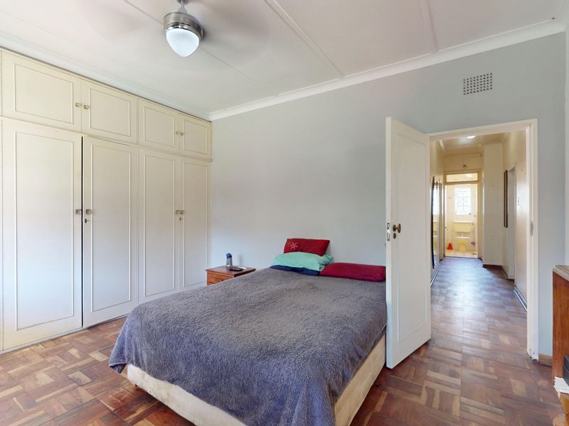A bedroom featuring classic parquet flooring, extensive built-in cabinetry, and a ceiling fan, with a view leading into the hallway.