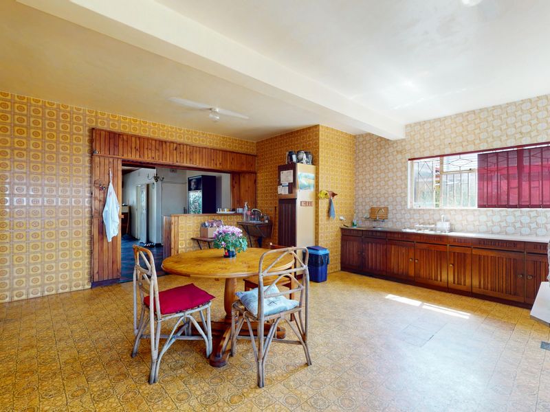 Spacious kitchen featuring dated wooden cabinetry, patterned wall tiles, and vinyl flooring, offering significant potential for a modern renovation.