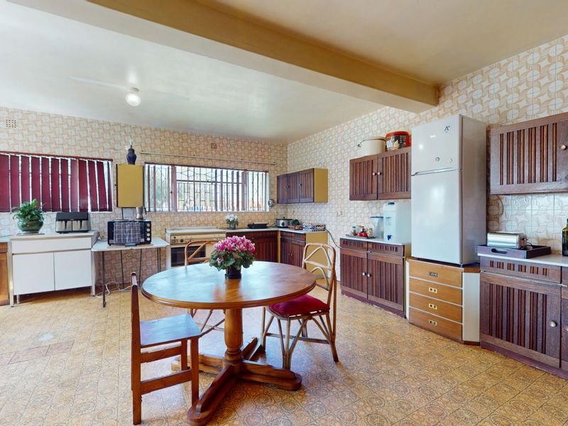 Spacious open-plan kitchen and dining area featuring extensive built-in wooden cabinetry and traditional tiled finishes, offering significant potential for modern renovation.