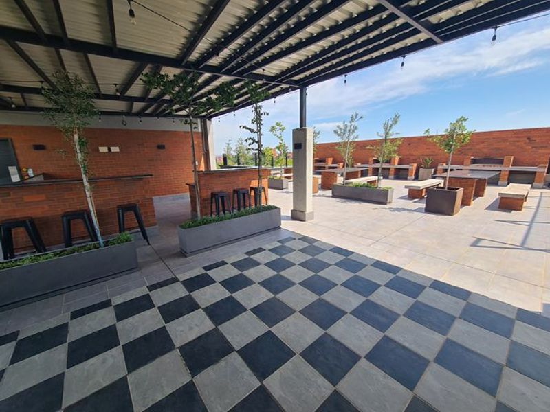 Spacious covered outdoor patio featuring brick walls, checkerboard tiled flooring, and built-in counters, ideal for entertaining and social gatherings.