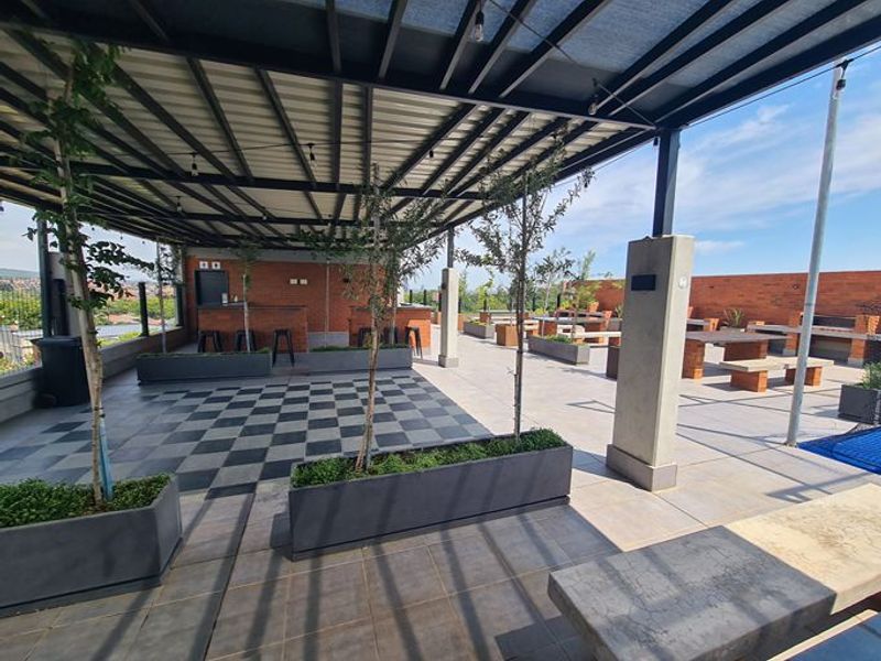 Spacious covered rooftop patio featuring a built-in brick bar, integrated braai area, and modern tiled flooring, ideal for outdoor entertaining.