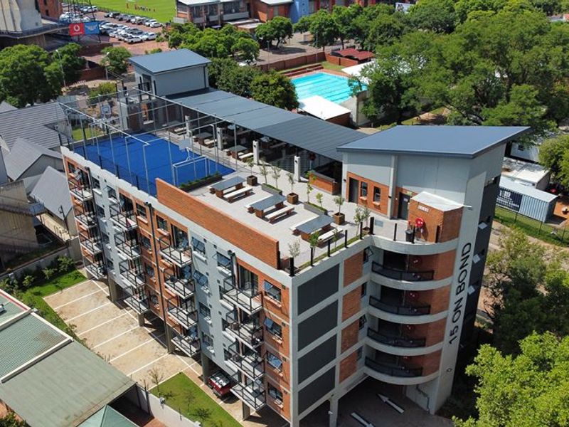 Aerial view of a multi-story apartment building featuring a rooftop sports court, communal terrace, and private balconies.