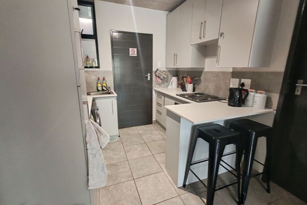 Modern kitchen featuring light grey cabinetry, stone countertops, an electric hob, and tiled flooring, complemented by an exposed concrete ceiling.