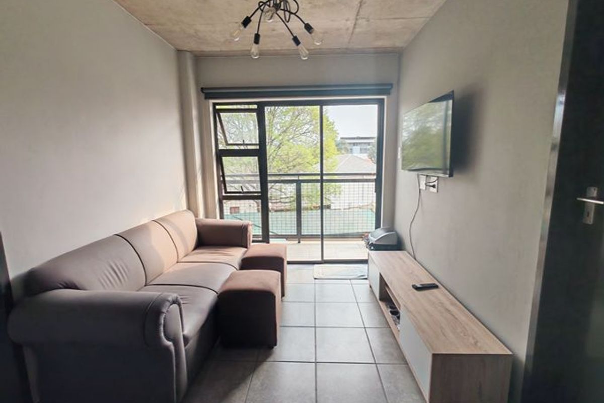 A compact living room featuring an exposed concrete ceiling, tiled floors, and direct access to a balcony through a sliding glass door.