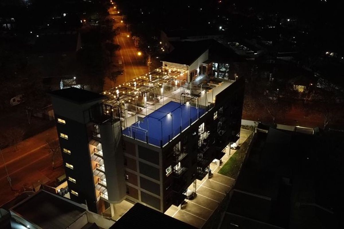 Nighttime aerial view of an apartment building featuring a rooftop sports facility and ground-level parking.