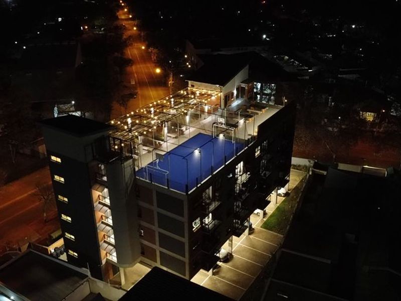 Nighttime aerial view of an apartment building featuring a rooftop sports facility and ground-level parking.