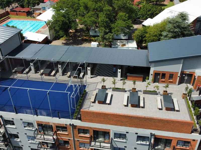 Aerial view of an apartment building rooftop featuring a sports court, covered terrace area, and landscaped planters.