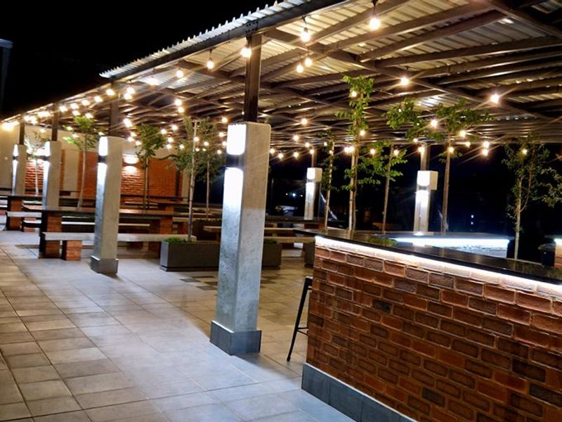 Spacious covered outdoor patio featuring a brick bar counter, concrete pillars, tiled flooring, and integrated string lighting for evening ambiance.