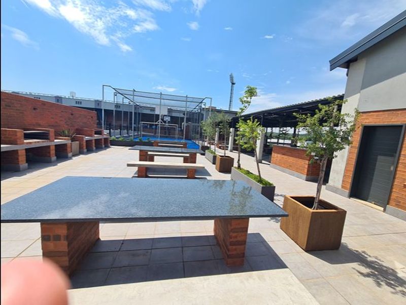 Spacious outdoor patio area featuring built-in brick braai stations, granite-topped dining tables, and paved flooring, ideal for communal entertainment.