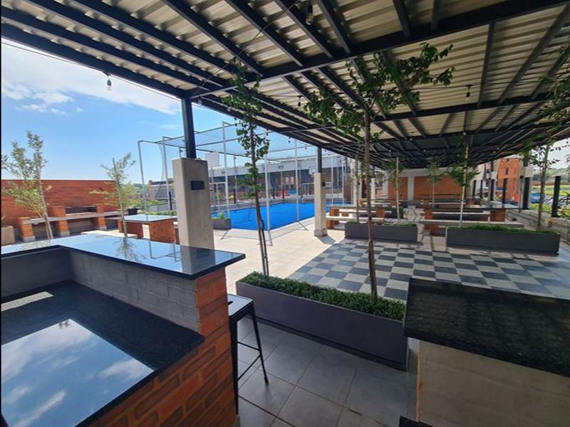 Spacious covered outdoor patio featuring a built-in braai area with granite countertops, brick masonry, and integrated planters, overlooking a sports facility.