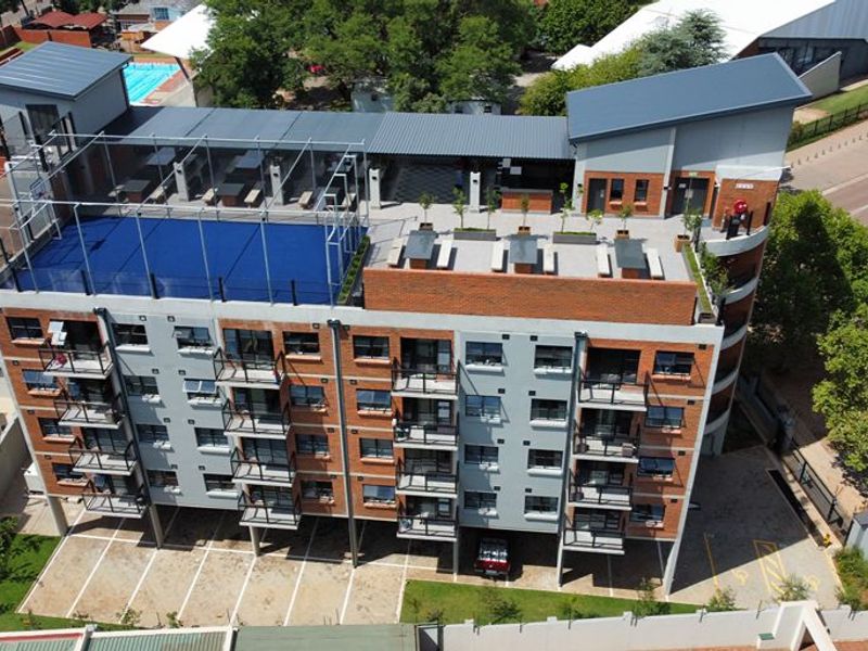 Aerial view of a modern multi-story apartment building featuring a rooftop sports court, communal terrace, and private balconies.