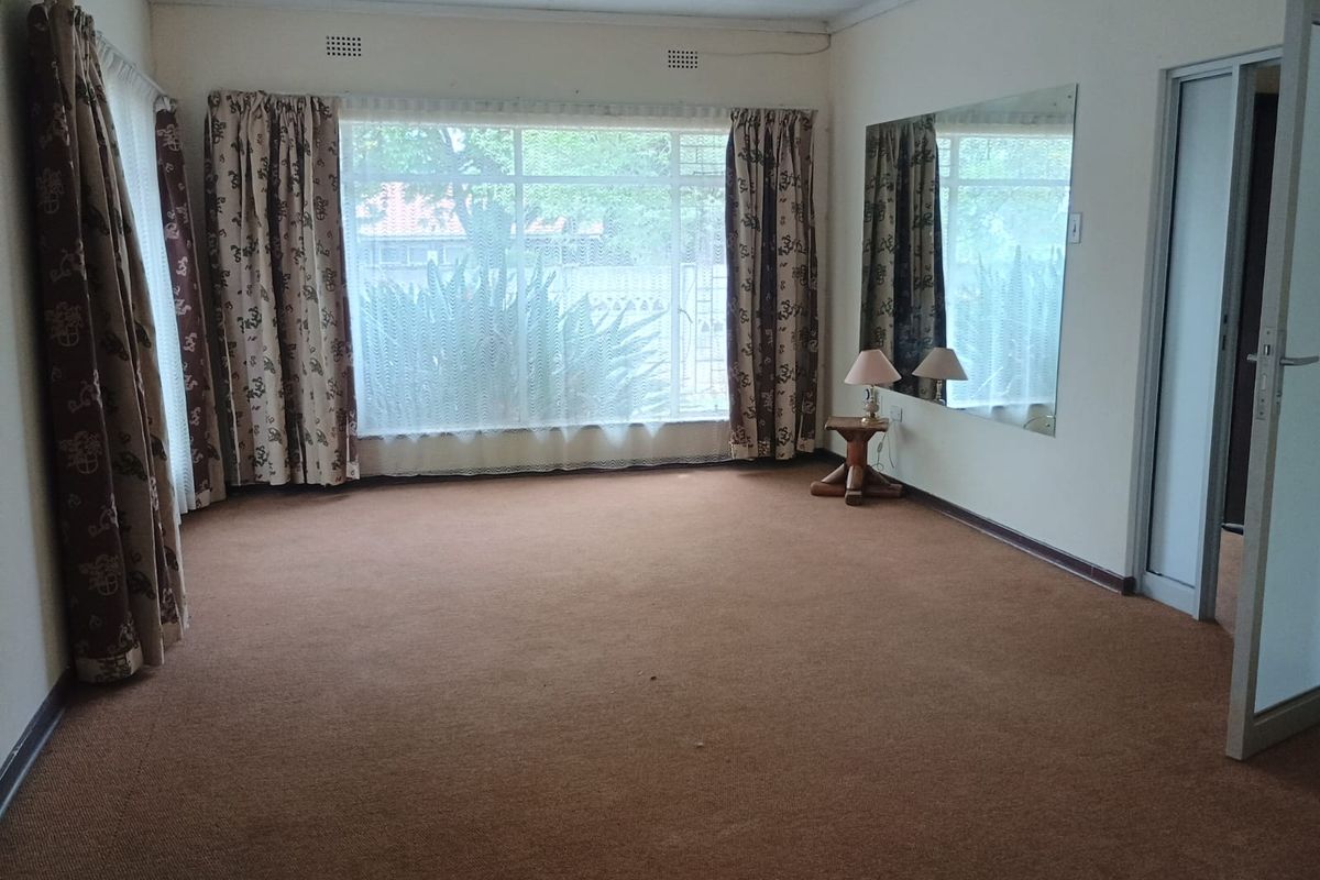 Spacious living area featuring large windows, wall-to-wall carpeting, and a wall-mounted mirror, offering a blank canvas for renovation.