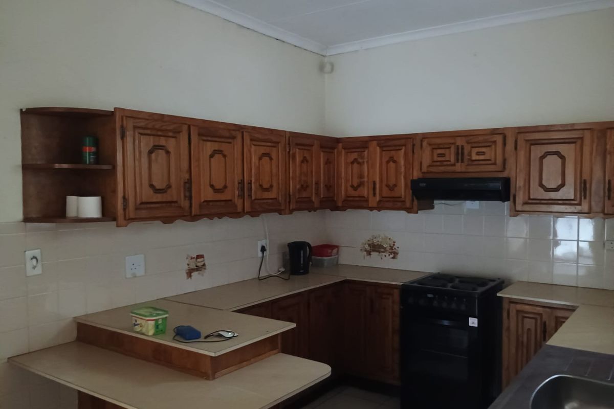 A functional kitchen featuring traditional wooden cabinetry, laminate countertops, tiled backsplash, and a freestanding stove with an extractor fan.