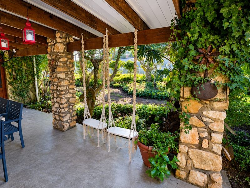 A charming covered patio featuring rustic stone pillars and exposed timber beams, overlooking a lush, well-maintained garden area.
