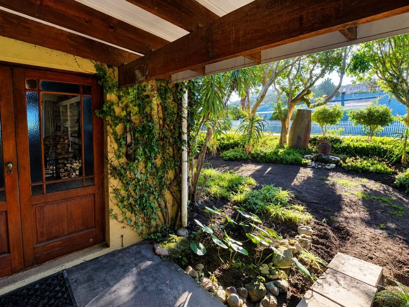 A covered patio area featuring exposed timber beams and a classic timber-framed entrance door, overlooking a well-established garden.