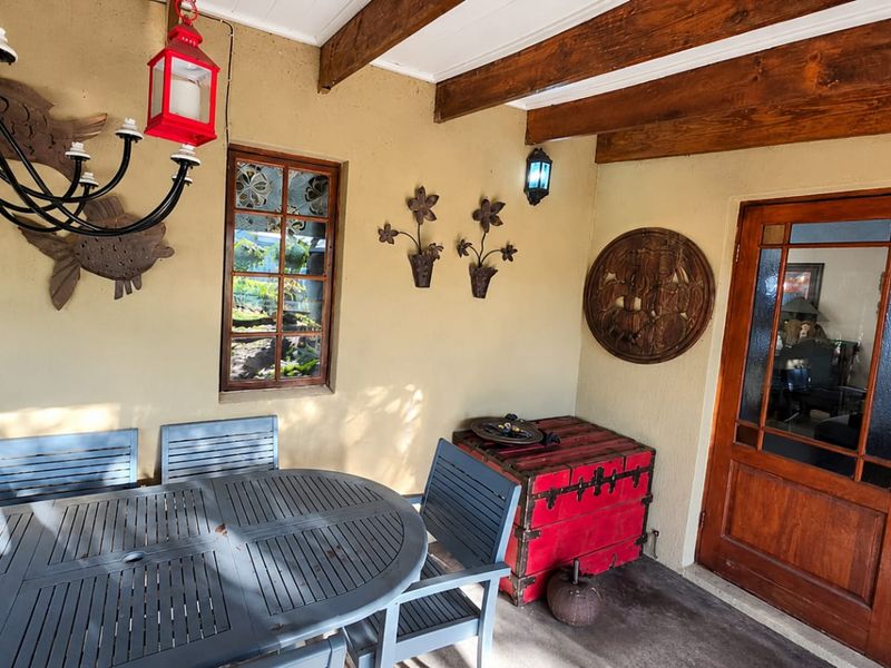 A covered patio area featuring exposed timber ceiling beams, concrete flooring, and a classic timber-framed glass door leading into the home.