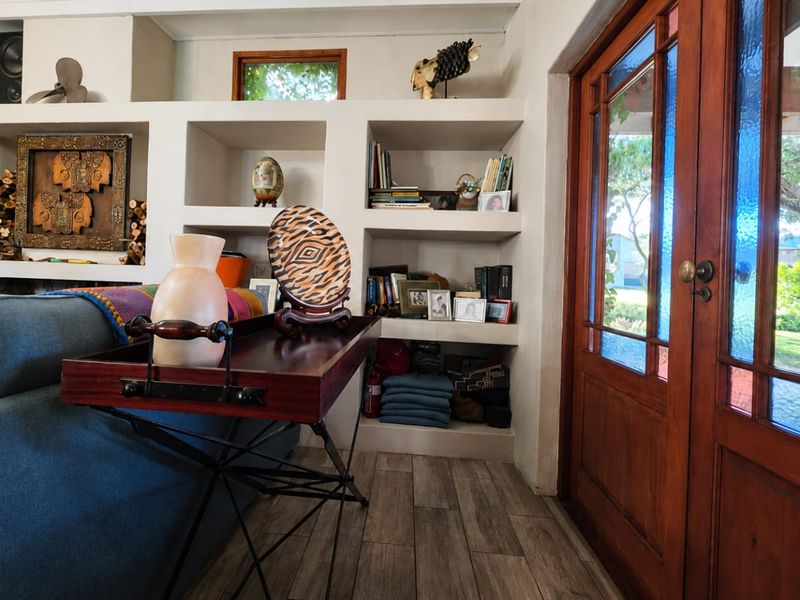 Living room featuring built-in wall shelving, wood-look tile flooring, and timber-framed glass double doors providing natural light and garden access.