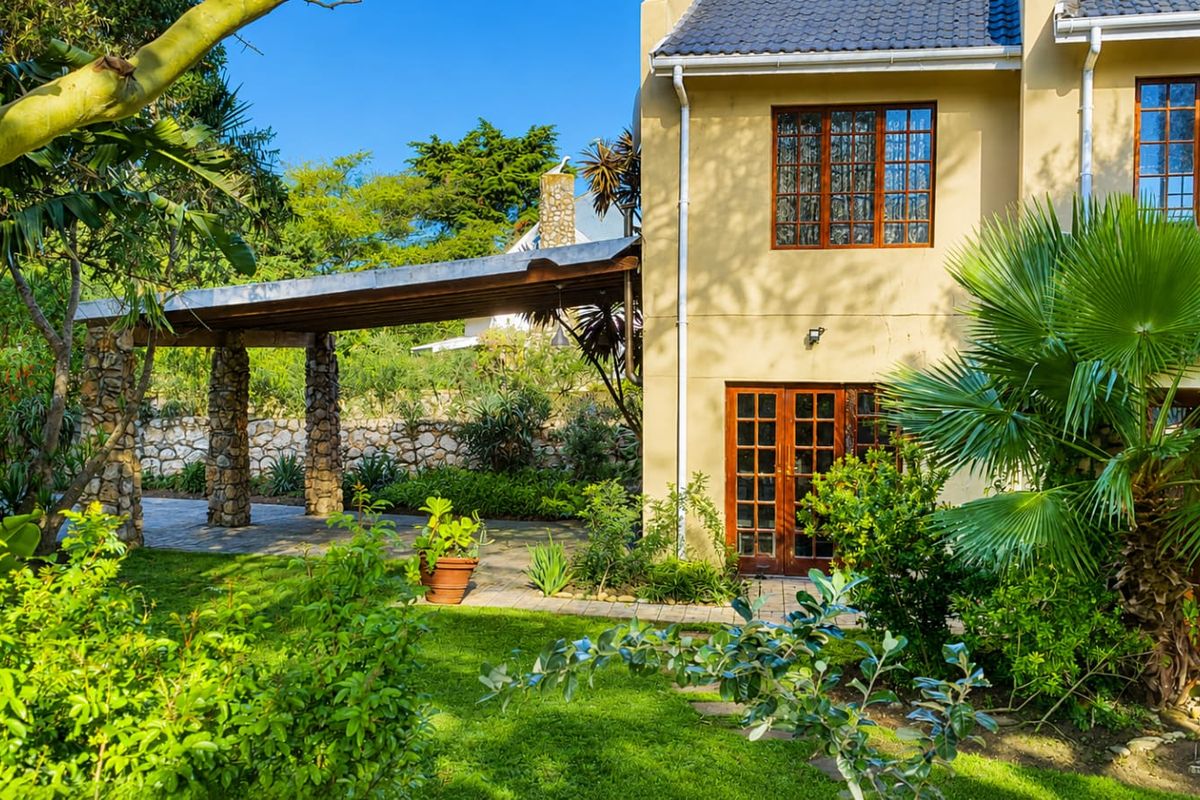 A well-maintained rear exterior featuring a covered patio with stone pillars, timber-framed doors and windows, and a lush, landscaped garden setting.