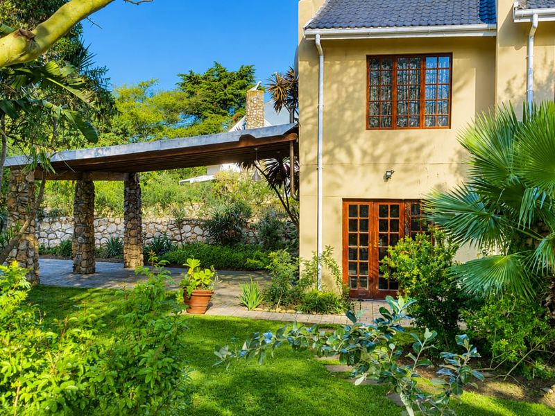 A well-maintained rear exterior featuring a covered patio with stone pillars, timber-framed doors and windows, and a lush, landscaped garden setting.