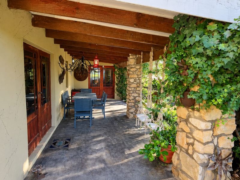 A covered patio area featuring exposed timber beams, a stone-clad support pillar, and direct access to the home through timber-framed double doors.